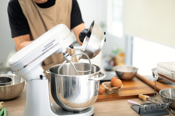 Male baker pouring ingredients into a stand mixer for cookie dough
