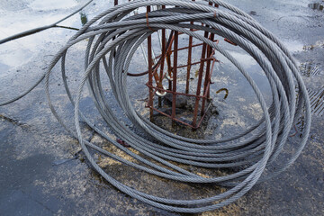 Coiled Steel Cables - Gray Steel Wire Rope and Rusty Reinforcement Bars on Wet Concrete Texture After Rain