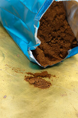 Freshly ground coffee poured onto a golden surface from a shiny blue bag. Gusset Packaging. Brass surface. Copy space.