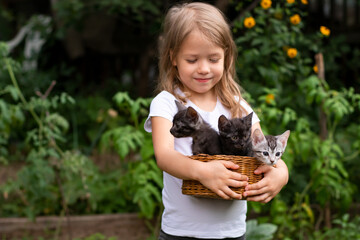 smiling little girl holding a basket with small kittens outdoors in nature