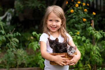 smiling little girl looking at camera and holding a basket with small kittens outdoors in nature