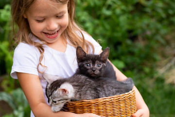 smiling little girl holding a basket with small kittens outdoors in nature