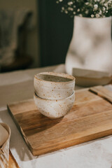Two white bowls on a wooden cutting board. The bowls are placed on the board and are not touching each other