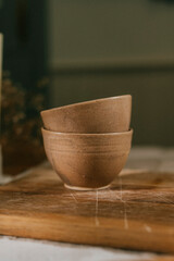 Two brown ceramic bowls sit on a wooden cutting board. The bowls are placed close together, and the cutting board is made of wood. Concept of warmth and coziness, as the wooden cutting board