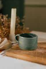 A candle is lit next to a green ceramic mug. The candle is yellow and the mug is blue