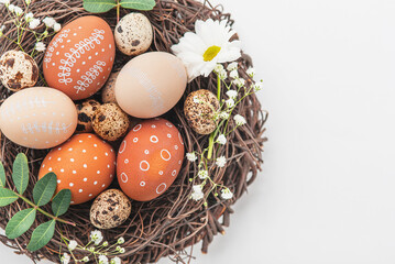Easter nest with hand-painted eggs and quail eggs on a light background. A rustic spring composition with natural elements, fresh greenery and floral details.