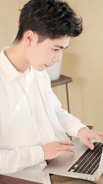 自宅やカフェなどでノートパソコンで作業する若い大学生のような男性の縦動画　AIなどを使って時短するイメージ