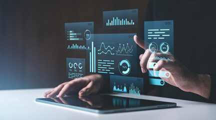 Interactive digital data visualization panels being accessed by a hand on a tablet on a dark...