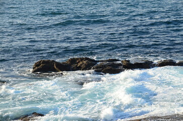 Obraz premium Powerful waves crashing against rugged coastal rocks on the Baiona coast in southern Galicia, creating a striking mix of blue water and white foam 