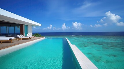 Fototapeta premium The image shows a beautiful modern luxury villa with a stunning view of the ocean. The villa is located on a sandy beach with crystal clear blue water and white sand. The sky is a beautiful