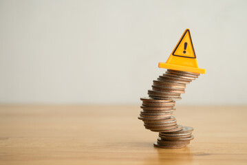 Warning sign label on stack coins in uncertainty situation on wooden table with white background...