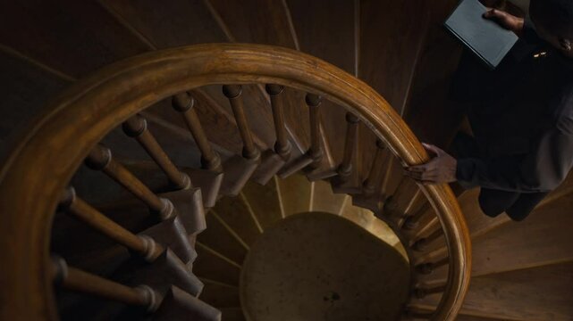 High angle view of African American catholic priest with holy bible going up wooden stairs holding winding banister in church