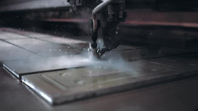 Slow-motion close-up of a metal cutting machine slicing through thick steel, sending sparks and steam into the air in an industrial setting.