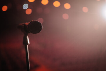 Obraz premium A microphone on a stand with dramatic stage lighting and blurred bokeh lights in the background, creating a moody atmosphere..