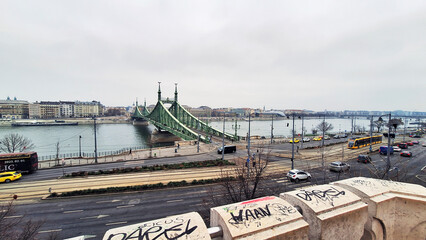 View of the road and tramway lines of Pest with the Liberty Bridge seen from the Gellert Hill rock chapel at a winter sunset. Buda cityscape on the other side of the Danube River, Budapest, Hungary.