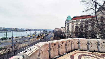 Street and tramway lines of Pest with the Liberty Bridge at the left end seen from the Rock Chapel on Gellert Hill at a winter sunset. Buda on the left rear side of the Danube bank, Budapest, Hungary.