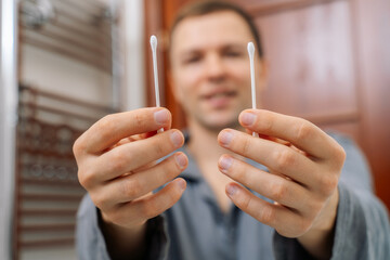 The man is holding hygienic cotton buds in his hands, close-up. The concept of body hygiene.