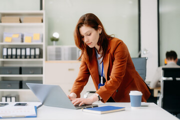 Obraz premium Confident business expert attractive smiling young woman typing laptop and holding digital tablet on desk