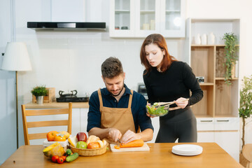 Discover a joyful couple preparing fresh vegetables, embracing healthy eating and teamwork in a...