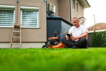 Gardener taking break on lawn and browsing smartphone