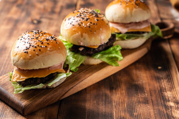 Three burgers with patty, cheese and lettuce on a wooden board and background. Close-up. Space for text.