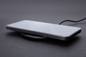 Mobile smart phone on wireless charging device on dark background. smartphones connected to power...