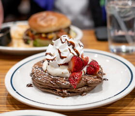 Chocolate pancakes topped with whipped cream and strawberries in restaurant diner