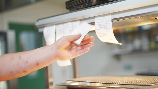 A person is reaching for a stack of receipts on a counter. The receipts are numbered and appear to be for a restaurant