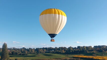 Obraz premium Yellow and white hot air balloon flying high in the clear blue sky over a green rural landscape.