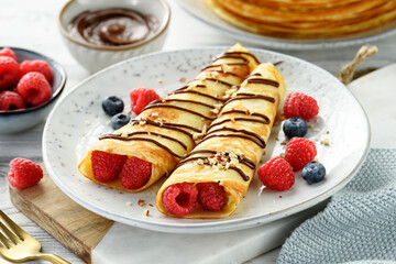 Thin pancakes or crepes with cottage cheese filling, fresh berries and chocolate sauce , sprinkled with nuts