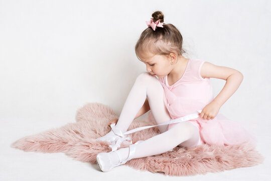 Little girl in a pink costume learning to tie ballet shoes