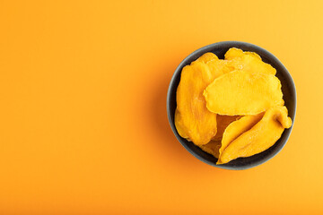 Dried Mango in blue ceramic bowl on orange pastel paper. Top view, copy space