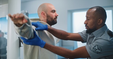 Security Checkpoint in Airport Terminal: African American Security Officer Checks Adult Man for...