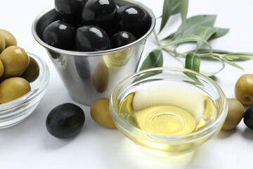 Bowl of fresh olive oil and olives with leaves on the table
