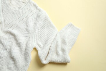 White knitted sweater on paper color background top view copy space. Texture of woolen cotton winter autumn cozy sweater, clothes. Knitted jumper, pullover, fashion. Sweater close-up