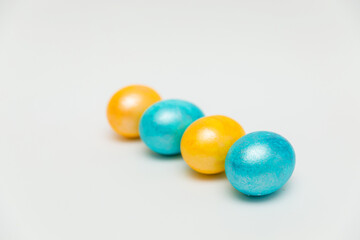 Four vibrantly colored Easter eggs, two yellow and two blue, arranged in a diagonal line on a clean white background, creating a festive and minimalist composition.