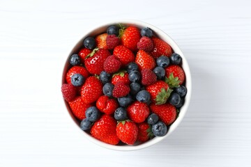 Different fresh ripe berries in bowl on wooden table, top view