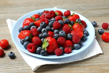 Different fresh ripe berries in bowl on wooden table