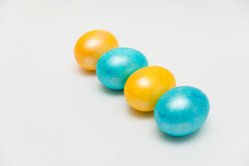 Four vibrantly colored Easter eggs, two yellow and two blue, arranged in a diagonal line on a clean white background, creating a festive and minimalist composition.