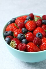Different fresh ripe berries in bowl on gray table