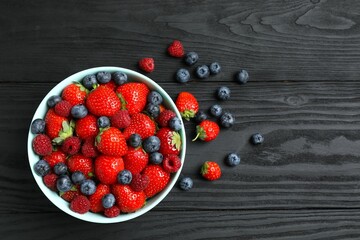 Different fresh ripe berries in bowl on wooden table, top view