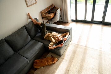 Happy smiling young student woman lying on couch, listening music in headphones and enjoying....