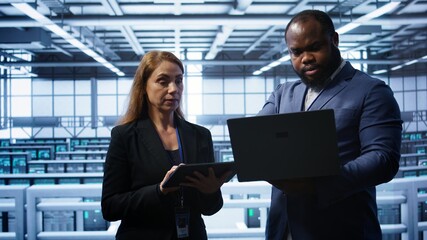 Coworkers doing yearly maintenance using tablet and laptop to prolong data center equipment life...