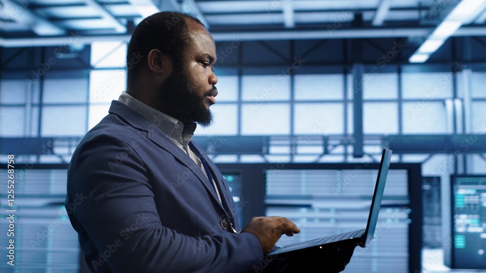 Poster african american man walking in high tech facility, using laptop to patch network issues leading to 
