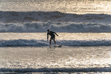 A lone surfer skillfully and gracefully navigates the shimmering waves during a stunningly beautiful sunset at the tranquil beach, creating a picturesque scene, Bali, Indonesia