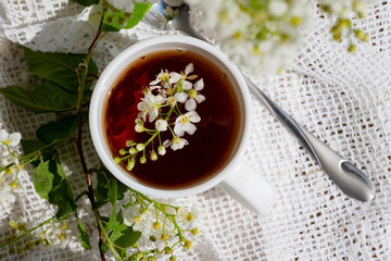 Delicate white flowers float on top of a steaming cup of tea surrounded by greenery on a sunny day