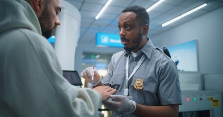 Fototapeta premium Airport Terminal: African American Security Officer Conducts TSA Hand Swab Screening with Brush to Adult Man for Plane Flight. ETD Procedure to Identify Traces of Explosive Materials. Medium Close Up.
