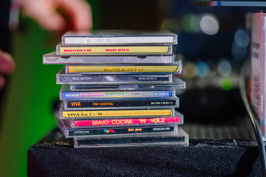 Stack of colorful CD cases on a table with blurred background, featuring various album titles under bright lighting.