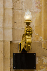 Golden Angel Shaped Lamp Ornament Affixed to Rustic Stone Wall Interior