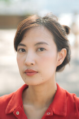 Fototapeta premium Asian thoughtful woman in red shirt gazes directly at camera, with soft natural light highlighting her features